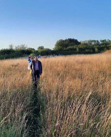 Begeleide groep wandelt in een rij door hoog, goudkleurig gras